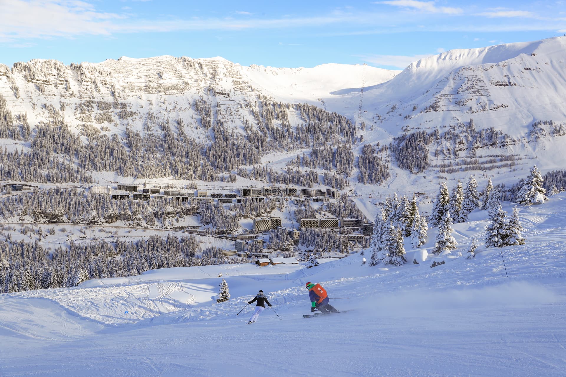 Skiiers skiing down slope into Flaine ski resort on bluebird day